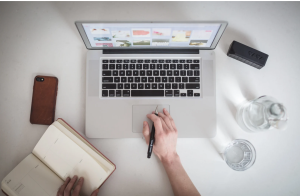 A laptop, phone, notebook and glass of water with a person doing SEO work